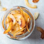 Homemade coconut chips in glass jar, gray background, top view. Vegan food concept.