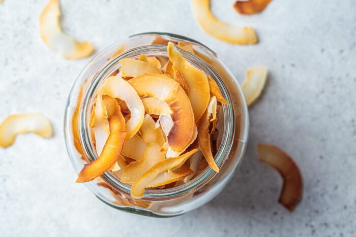 Homemade coconut chips in glass jar, gray background, top view. Vegan food concept.